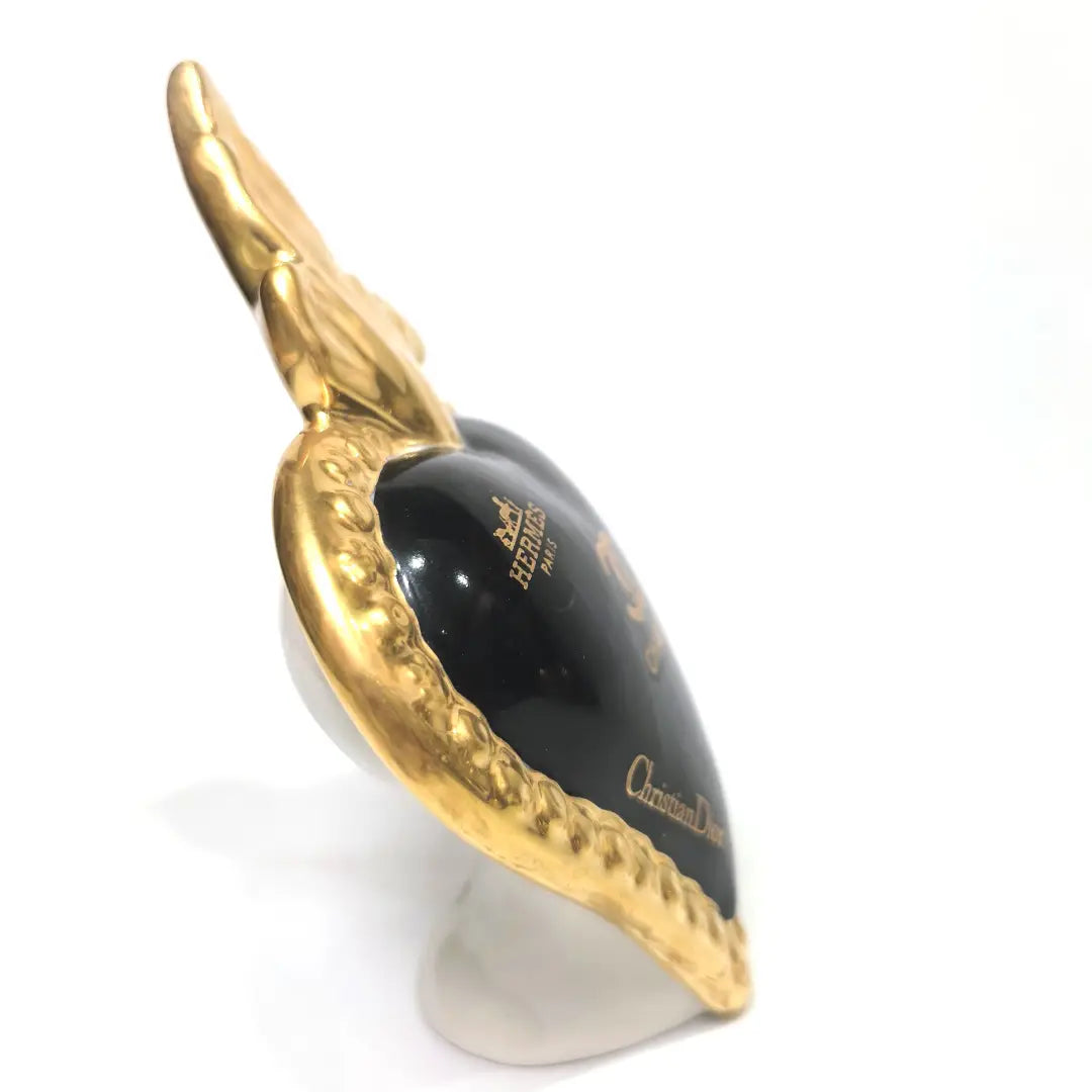 Scultura a forma di Cuore Sacro in ceramica nera lucida, impreziosita da una ricca cornice dorata lavorata a sbalzo e decorata con loghi fashion iconici in oro. Questo esclusivo oggetto d'arredo in stile pop art presenta una fiamma superiore dorata e una base d'appoggio integrata, perfetto per aggiungere un dettaglio di lusso moderno agli ambienti interni.
