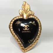 Scultura a forma di Cuore Sacro in ceramica nera lucida, impreziosita da una ricca cornice dorata lavorata a sbalzo e decorata con loghi fashion iconici in oro. Questo esclusivo oggetto d'arredo in stile pop art presenta una fiamma superiore dorata e una base d'appoggio integrata, perfetto per aggiungere un dettaglio di lusso moderno agli ambienti interni.