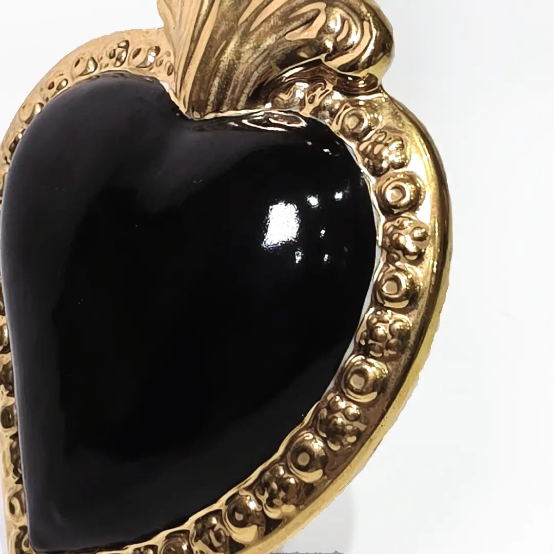 Scultura a forma di Cuore Sacro in ceramica nera lucida, incorniciata da un elegante bordo dorato con decorazioni a rilievo e completata da una fiamma superiore in oro. Questo oggetto di design artigianale con base d'appoggio è un complemento d'arredo raffinato, ideale per arricchire ambienti moderni con un tocco di arte sacra contemporanea.
