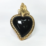 Scultura a forma di Cuore Sacro in ceramica nera lucida, incorniciata da un elegante bordo dorato con decorazioni a rilievo e completata da una fiamma superiore in oro. Questo oggetto di design artigianale con base d'appoggio è un complemento d'arredo raffinato, ideale per arricchire ambienti moderni con un tocco di arte sacra contemporanea.