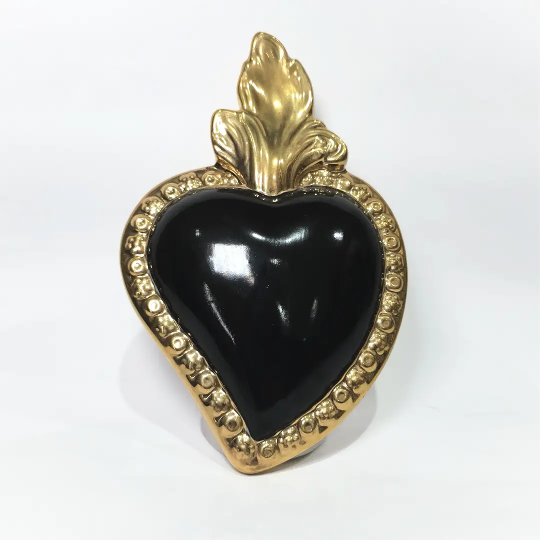 Scultura a forma di Cuore Sacro in ceramica nera lucida, incorniciata da un elegante bordo dorato con decorazioni a rilievo e completata da una fiamma superiore in oro. Questo oggetto di design artigianale con base d'appoggio è un complemento d'arredo raffinato, ideale per arricchire ambienti moderni con un tocco di arte sacra contemporanea.