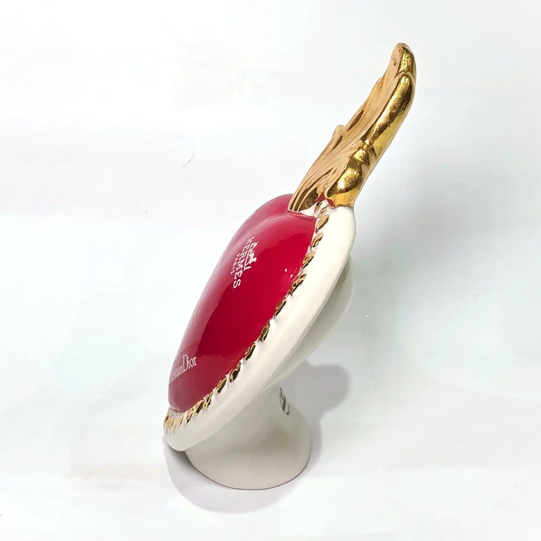 Scultura decorativa a forma di Cuore Sacro in ceramica rossa lucida, arricchita da loghi fashion bianchi e una fiamma superiore dorata. Il design è completato da una cornice bianca perlinata con borchie oro, rendendo questo oggetto un complemento d'arredo pop art unico e di tendenza per la casa.