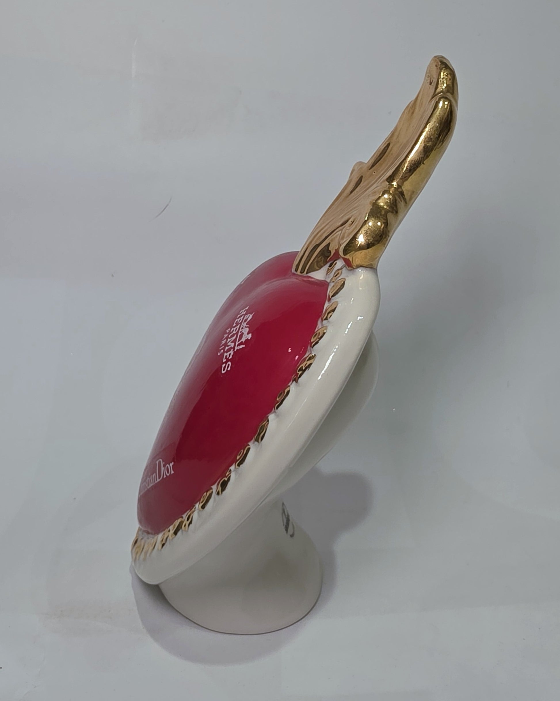Scultura decorativa a forma di Cuore Sacro in ceramica rossa lucida, arricchita da loghi fashion bianchi e una fiamma superiore dorata. Il design è completato da una cornice bianca perlinata con borchie oro, rendendo questo oggetto un complemento d'arredo pop art unico e di tendenza per la casa.