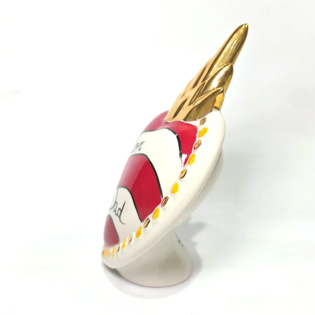 Scultura decorativa a forma di Cuore Sacro in ceramica rossa e bianca lucida, caratterizzata da un design a strisce orizzontali con le scritte "Mom" e "Dad" in corsivo nero. L'oggetto è completato da una corona superiore dorata e una cornice perlinata con dettagli gialli e borchie oro, rappresentando un complemento d'arredo affettivo e originale per la casa.