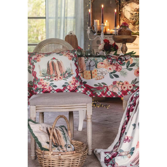 Cuscino natalizio Blanc Mariclo con stampa pandoro e ghirlanda di biscotti, appoggiato su una sedia vintage in legno. Sullo sfondo, tavola imbandita coordinata con candele e decorazioni shabby chic.