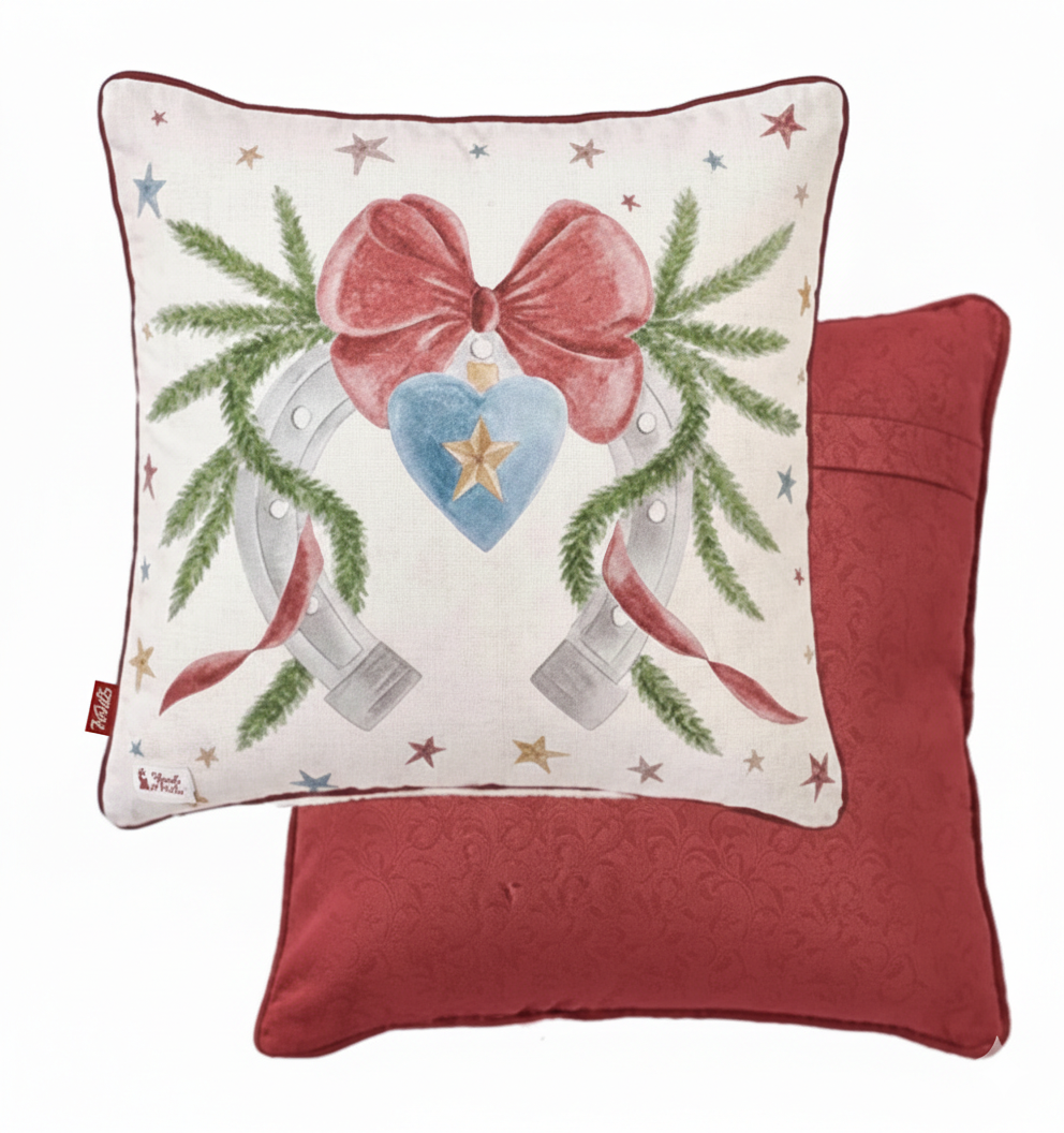 Cuscino natalizio Nuvole di Stoffa "La Giostra di Amelie" (Modello B). Il fronte mostra un ferro di cavallo decorato con ghirlande di pino, un fiocco rosso e un cuore azzurro centrale; il retro è di colore rosso intenso.