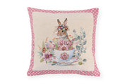 Cuscino pasquale Nuvole di Stoffa i con bordo a pois rosa. Decorazione centrale con illustrazioni vintage di coniglietti, tazze da tè fiorite e ghirlande. Tessuto elegante per la tavola di Pasqua 2026.