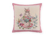 Cuscino pasquale Nuvole di Stoffa i con bordo a pois rosa. Decorazione centrale con illustrazioni vintage di coniglietti, tazze da tè fiorite e ghirlande. Tessuto elegante per la tavola di Pasqua 2026.