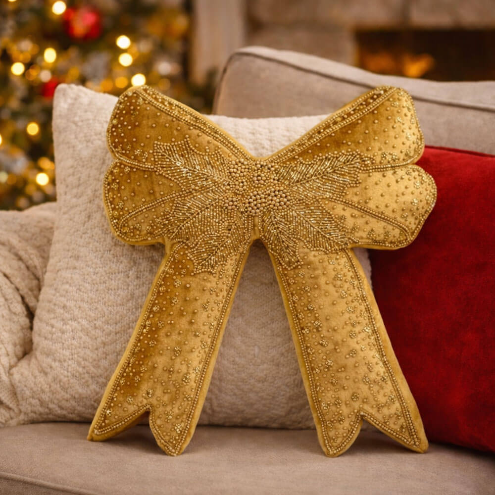 Cuscino a forma di fiocco Blanc Mariclò in velluto oro. Il dettaglio mostra un raffinato ricamo centrale a foglia di agrifoglio realizzato con perline dorate su una texture morbida.