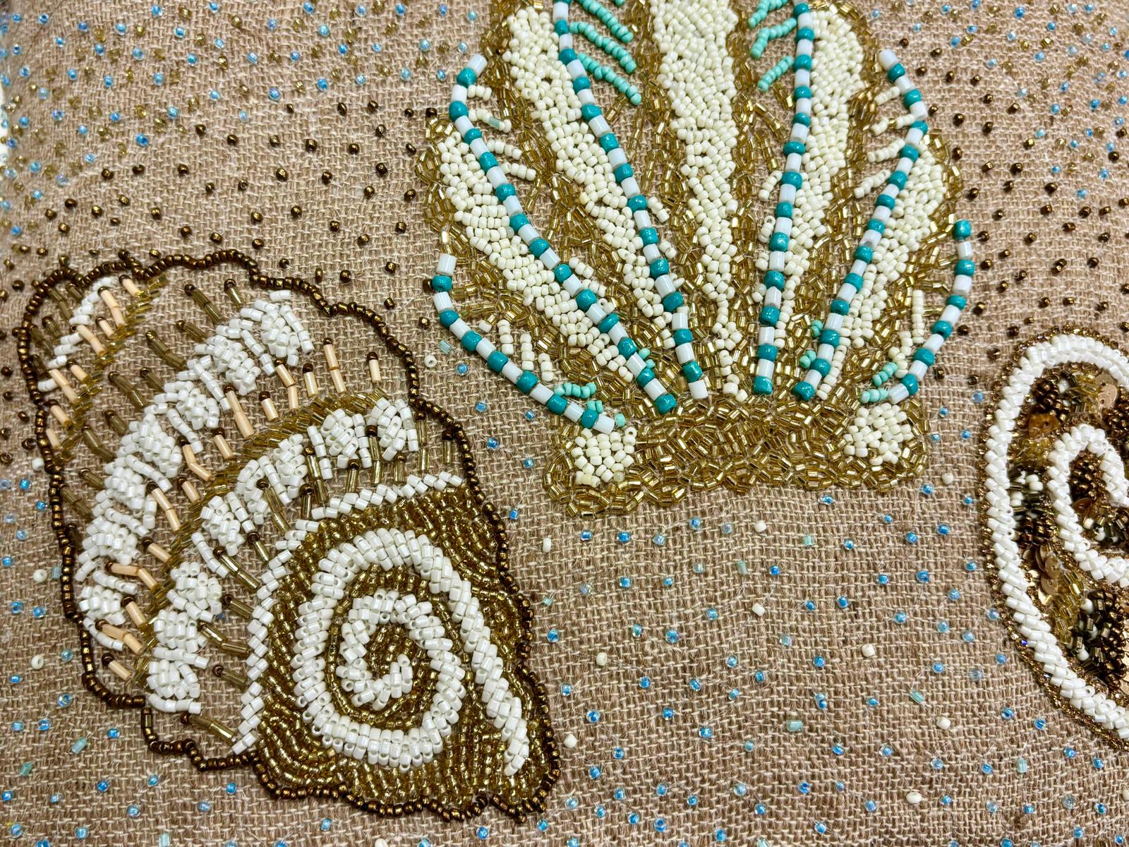 dettaglio del cuscino Blanc Mariclo' linea Maldive in lino naturale color beige. Stampa marina con conchiglie ricamate sabbia e azzurro. Complemento d'arredo per case estive.