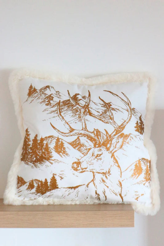 Cuscino natalizio bianco Blanc Mariclò con stampa cervo dorata e bordo in pelliccia, esposto su una mensola in legno chiaro in un interno moderno e luminoso. Design elegante La Fable Dorée.