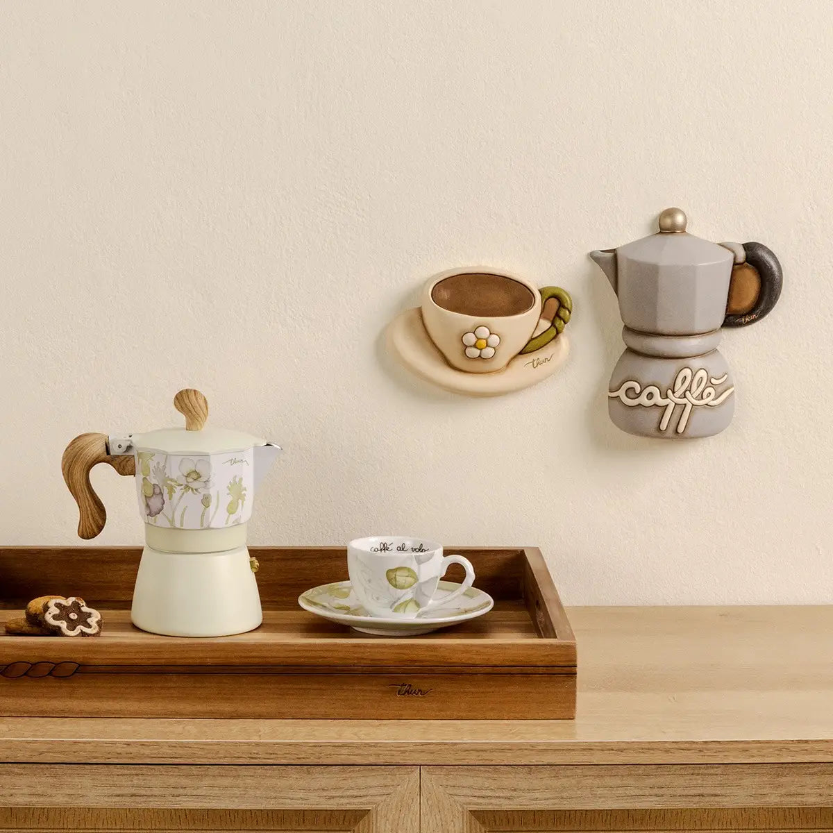 Formella decorativa da parete in ceramica firmata Thun, sagomata a forma di tazzina da caffè con piattino nei delicati toni del beige e del marrone. Questo articolo della linea Country Bloom presenta un fiore bianco a rilievo al centro, un manico verde e il classico marchio Thun dorato sul piattino.