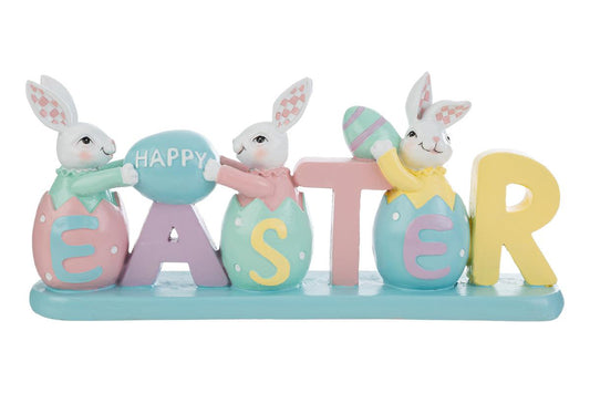 Decorazione pasquale con scritta "EASTER" color pastello e tre coniglietti bianchi. I coniglietti sono inseriti all'interno delle lettere a forma di uovo; i primi due sorreggono un uovo azzurro con la scritta "HAPPY". Statuina decorativa del marchio Le Stelle in resina colorata con dettagli rosa, gialli e verde menta su base azzurra.