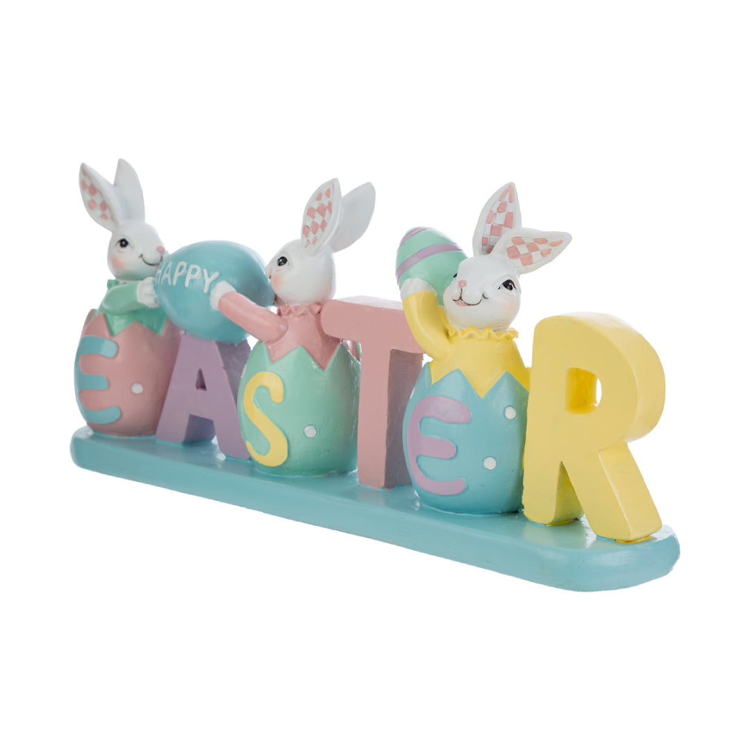 Decorazione pasquale con scritta "EASTER" color pastello e tre coniglietti bianchi. I coniglietti sono inseriti all'interno delle lettere a forma di uovo; i primi due sorreggono un uovo azzurro con la scritta "HAPPY". Statuina decorativa del marchio Le Stelle in resina colorata con dettagli rosa, gialli e verde menta su base azzurra.