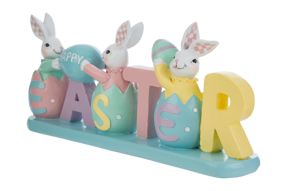 Decorazione pasquale con scritta "EASTER" color pastello e tre coniglietti bianchi. I coniglietti sono inseriti all'interno delle lettere a forma di uovo; i primi due sorreggono un uovo azzurro con la scritta "HAPPY". Statuina decorativa del marchio Le Stelle in resina colorata con dettagli rosa, gialli e verde menta su base azzurra.