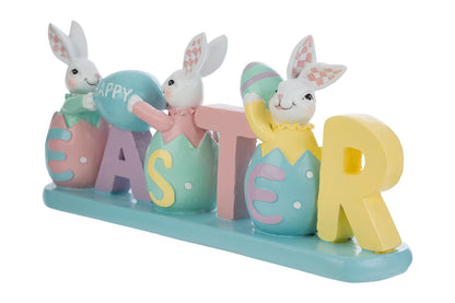Decorazione pasquale con scritta "EASTER" color pastello e tre coniglietti bianchi. I coniglietti sono inseriti all'interno delle lettere a forma di uovo; i primi due sorreggono un uovo azzurro con la scritta "HAPPY". Statuina decorativa del marchio Le Stelle in resina colorata con dettagli rosa, gialli e verde menta su base azzurra.
