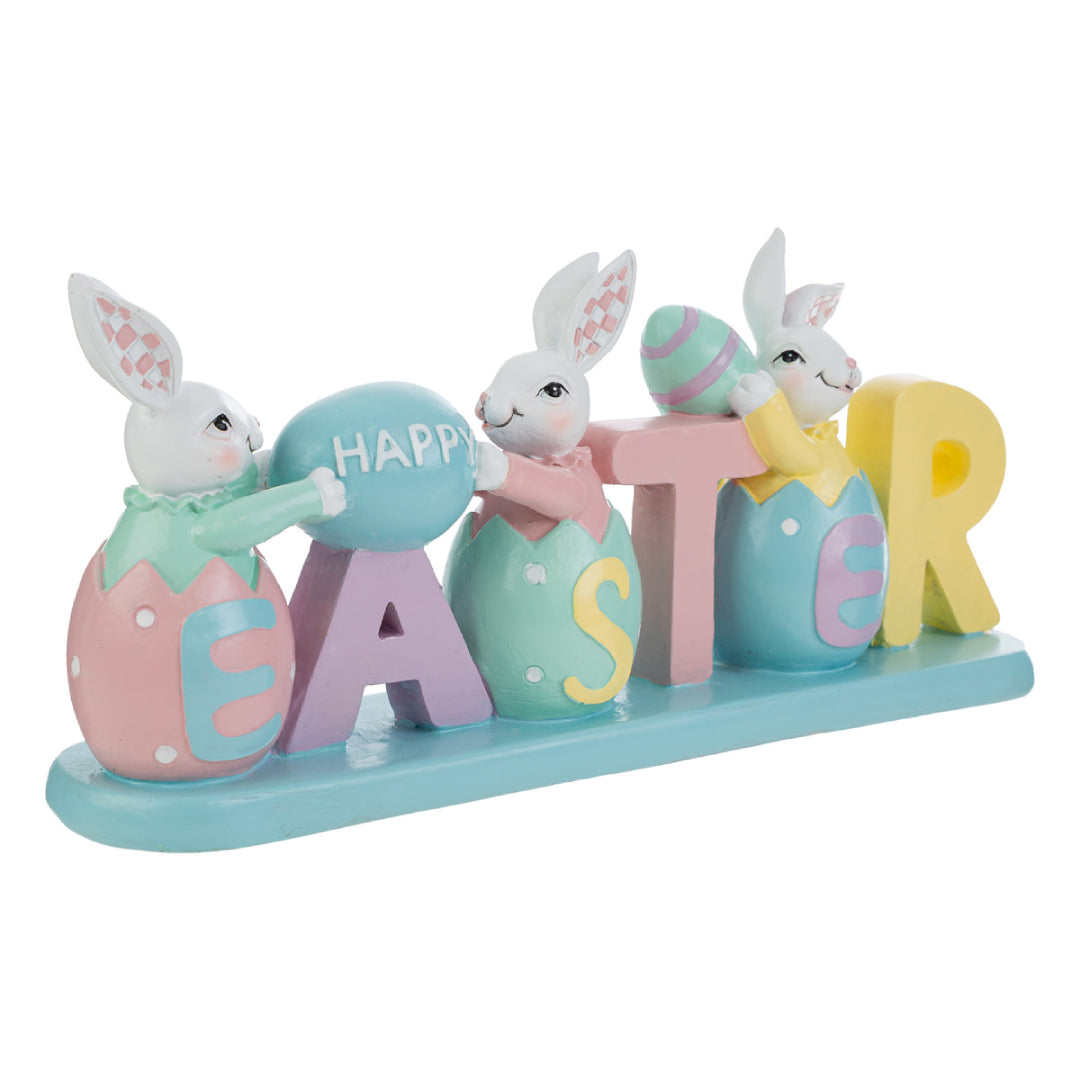 Decorazione pasquale con scritta "EASTER" color pastello e tre coniglietti bianchi. I coniglietti sono inseriti all'interno delle lettere a forma di uovo; i primi due sorreggono un uovo azzurro con la scritta "HAPPY". Statuina decorativa del marchio Le Stelle in resina colorata con dettagli rosa, gialli e verde menta su base azzurra.