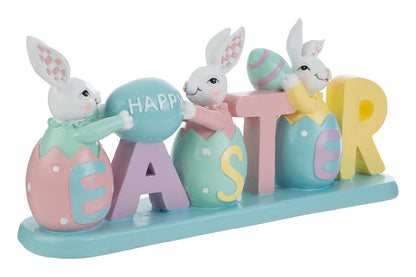 Decorazione pasquale con scritta "EASTER" color pastello e tre coniglietti bianchi. I coniglietti sono inseriti all'interno delle lettere a forma di uovo; i primi due sorreggono un uovo azzurro con la scritta "HAPPY". Statuina decorativa del marchio Le Stelle in resina colorata con dettagli rosa, gialli e verde menta su base azzurra.