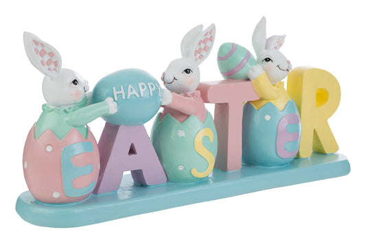 Decorazione pasquale con scritta "EASTER" color pastello e tre coniglietti bianchi. I coniglietti sono inseriti all'interno delle lettere a forma di uovo; i primi due sorreggono un uovo azzurro con la scritta "HAPPY". Statuina decorativa del marchio Le Stelle in resina colorata con dettagli rosa, gialli e verde menta su base azzurra.