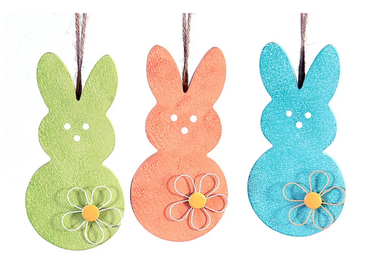 Tris di decorazioni pasquali pendenti in legno a forma di sagoma di coniglio. Il set comprende tre colori assortiti con finitura materica: verde mela, arancione e azzurro. Ogni coniglio è decorato con un fiore stilizzato in rilievo sulla base e presenta tre piccoli fori che disegnano il muso; sono appesi a un cordino di juta naturale.