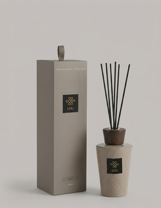 Il Diffusore per Ambienti Cuir Oud EDG è un set di profumazione per la casa composto da una boccetta con finitura intrecciata color tortora, un tappo in legno scuro e bastoncini neri. La scatola regalo coordinata a colonna con scritte dorate racchiude questa sofisticata fragranza legnosa, rendendola un complemento d'arredo perfetto per l'home decor moderno.