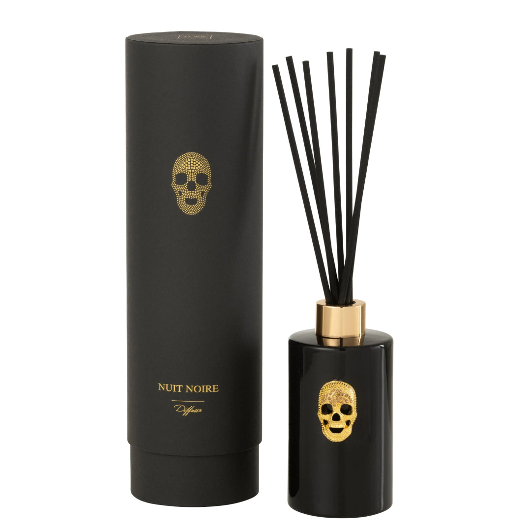 Diffusore di fragranza ad asta "Cranio" Nuit Noire firmato Jolipa, caratterizzato da una boccetta cilindrica in vetro nero lucido impreziosita da un dettaglio a rilievo dorato a forma di teschio e un colletto color oro abbinato. Questo esclusivo profumatore d'ambiente di design, completo di bastoncini neri, viene fornito con una raffinata confezione cilindrica coordinata total black con dettagli in oro, ideale per donare un tocco audace, moderno e sofisticato agli interni o come originale idea regalo