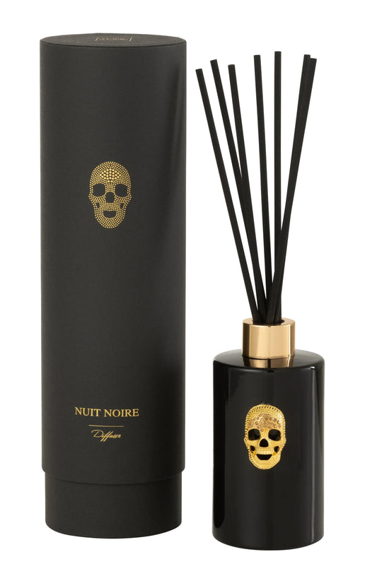 Diffusore di fragranza ad asta "Cranio" Nuit Noire firmato Jolipa, caratterizzato da una boccetta cilindrica in vetro nero lucido impreziosita da un dettaglio a rilievo dorato a forma di teschio e un colletto color oro abbinato. Questo esclusivo profumatore d'ambiente di design, completo di bastoncini neri, viene fornito con una raffinata confezione cilindrica coordinata total black con dettagli in oro, ideale per donare un tocco audace, moderno e sofisticato agli interni o come originale idea regalo