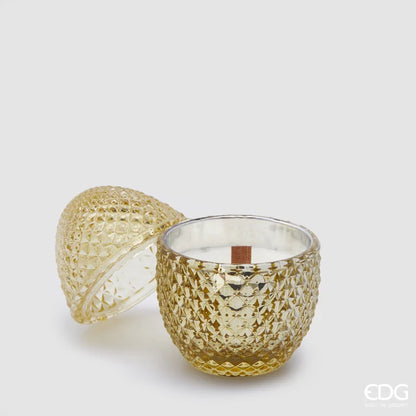 Candela profumata "L'Ove" alla fragranza Ginger & Warm Vanilla firmata EDG Enzo de Gasperi, caratterizzata da un elegante contenitore in vetro giallo ambrato lavorato a rilievo a forma di uovo con coperchio coordinato e stoppino in legno. Questa raffinata candela decorativa di lusso è accompagnata dalla sua confezione regalo gialla con motivi geometrici, ideale per profumare gli ambienti di casa con stile o come originale idea regalo home decor.