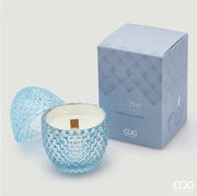 Candela profumata "L'Ove" alla fragranza Waterlilly & Rose firmata EDG Enzo de Gasperi, caratterizzata da un elegante contenitore in vetro celeste lavorato a rilievo a forma di uovo con coperchio coordinato e stoppino in legno. Questa raffinata candela decorativa di lusso è accompagnata dalla sua confezione regalo azzurra con motivi geometrici, ideale per profumare gli ambienti di casa con stile o come originale idea regalo home decor.