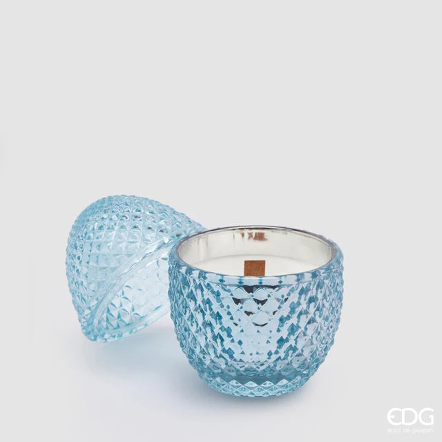 Candela profumata "L'Ove" alla fragranza Waterlilly & Rose firmata EDG Enzo de Gasperi, caratterizzata da un elegante contenitore in vetro celeste lavorato a rilievo a forma di uovo con coperchio coordinato e stoppino in legno. Questa raffinata candela decorativa di lusso è accompagnata dalla sua confezione regalo azzurra con motivi geometrici, ideale per profumare gli ambienti di casa con stile o come originale idea regalo home decor.