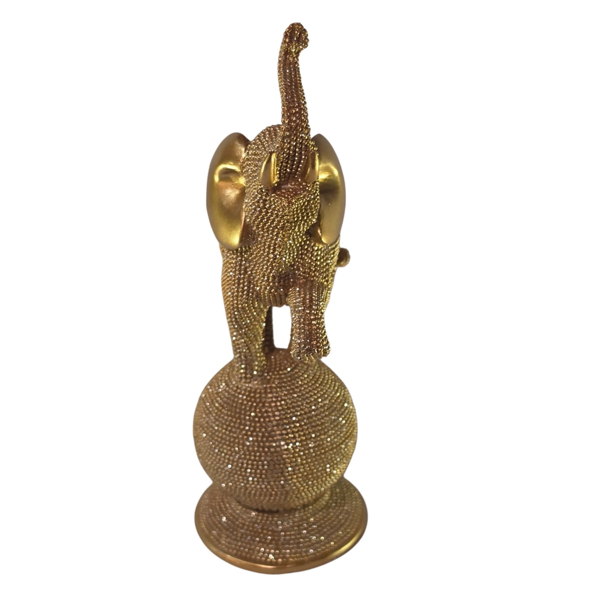 Statuina in resina raffigurante un elefante dorato in equilibrio su una sfera decorativa, con proboscide sollevata e orecchie lisce a effetto metallico, interamente ricoperto di brillantini glitterati. Oggetto decorativo scintillante firmato Sud Import, ideale come soprammobile portafortuna o idea regalo per la casa.
