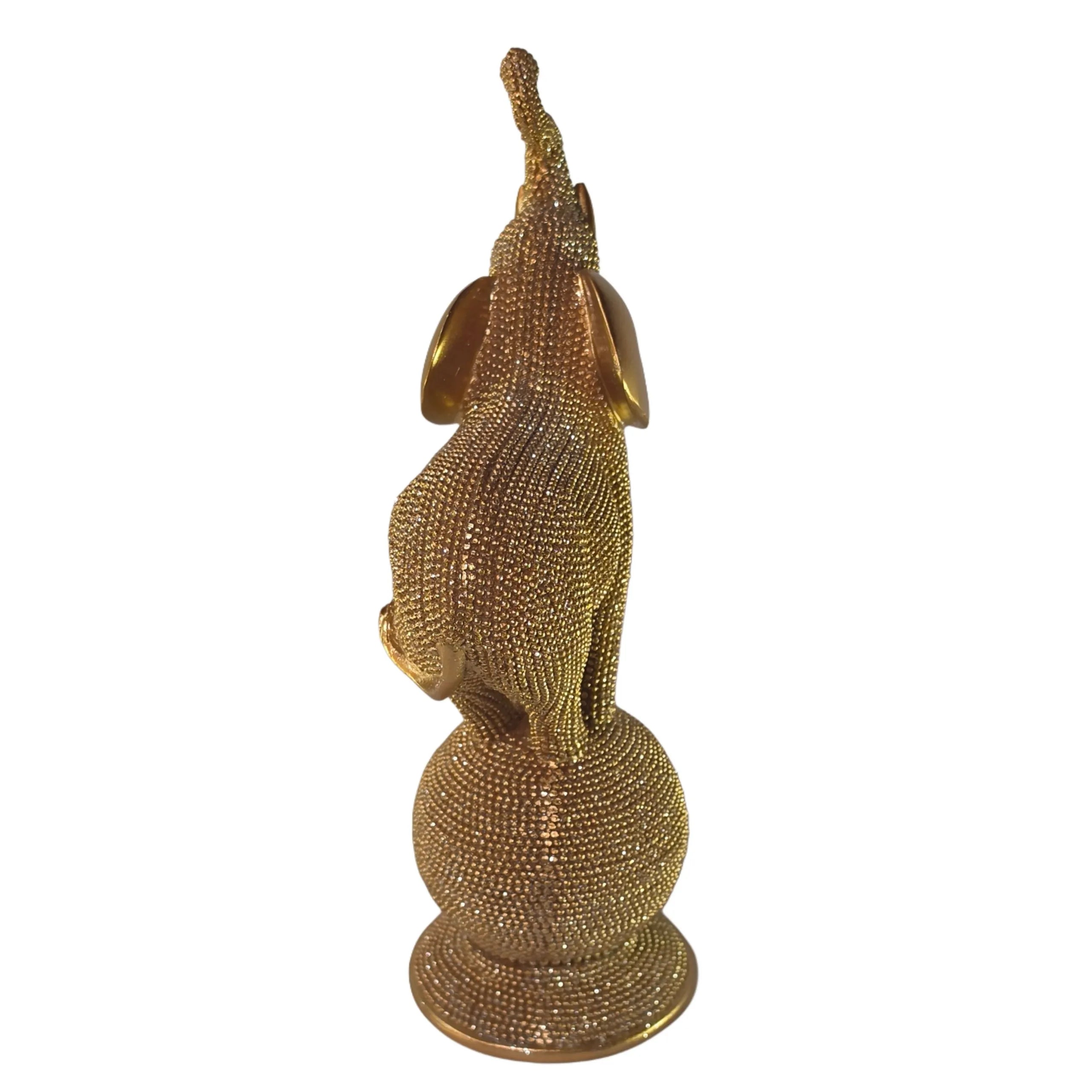 Statuina in resina raffigurante un elefante dorato in equilibrio su una sfera decorativa, con proboscide sollevata e orecchie lisce a effetto metallico, interamente ricoperto di brillantini glitterati. Oggetto decorativo scintillante firmato Sud Import, ideale come soprammobile portafortuna o idea regalo per la casa.