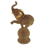 Statuina in resina raffigurante un elefante dorato in equilibrio su una sfera decorativa, con proboscide sollevata e orecchie lisce a effetto metallico, interamente ricoperto di brillantini glitterati. Oggetto decorativo scintillante firmato Sud Import, ideale come soprammobile portafortuna o idea regalo per la casa.