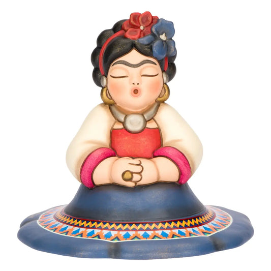 Statuina in ceramica Thun della collezione Frida Kahlo in formato medio, ritratta in una posa iconica con occhi chiusi e labbra socchiuse. La figura indossa abiti tradizionali messicani, tra cui una gonna blu decorata con motivi geometrici etnici e fiori colorati tra i capelli neri, rappresentando un pezzo da collezione ricco di fascino e significato culturale.