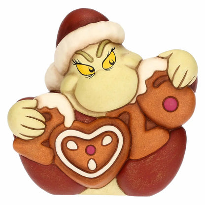 Un'iconica statuina in ceramica raffigura il Grinch in una versione stilizzata e decorativa. Il personaggio ha il volto di un verde tenue, con un’espressione imbronciata accentuata da sopracciglia folte e scure sopra grandi occhi gialli dalle pupille sottili. Indossa il classico cappello rosso da Babbo Natale con bordo e pompon bianco dall'aspetto soffice.