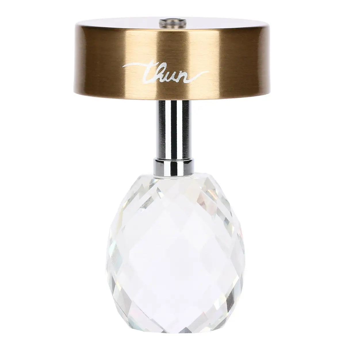Lampada da tavolo ricaricabile Thun con paralume cilindrico color oro e base in cristallo sfaccettato a forma di uovo color bianco. Lo stelo che unisce i due elementi è in metallo cromato e sul paralume è presente il logo Thun argentato.
