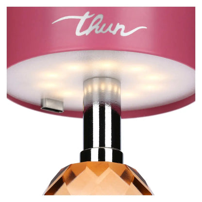 Inquadratura dal basso del paralume rosa che mostra il pannello LED circolare acceso, il quale emette una luce calda attraverso il diffusore bianco. Sono visibili anche la porta USB-C, lo stelo cromato e la parte superiore del cristallo arancione.