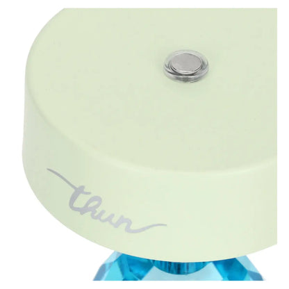 Vista ravvicinata dall'alto del paralume verde; al centro della parte superiore è visibile un piccolo pulsante metallico circolare con bordo trasparente, utilizzato per l'accensione e la regolazione.