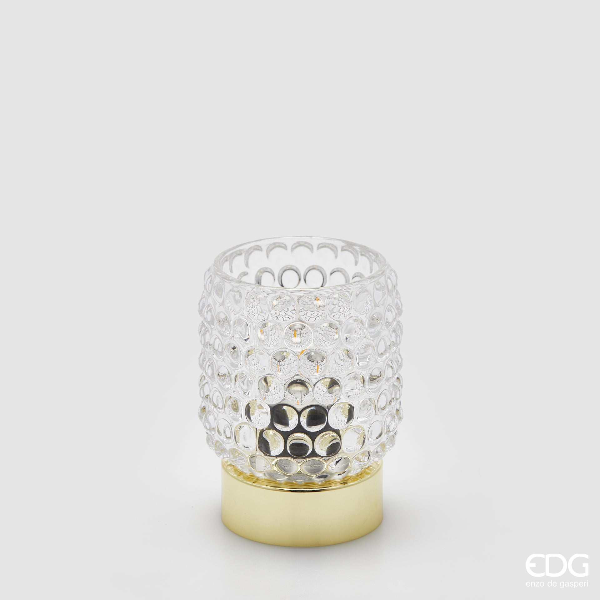 La lampada da tavolo Bubbles di Enzo De Gasperi (EDG) si distingue per un design raffinato che unisce un diffusore in vetro trasparente con un caratteristico motivo a rilievo a bolle e una base cilindrica in metallo dalla finitura dorata lucida. La particolare lavorazione del vetro permette alla luce di rifrangersi nell'ambiente in modo suggestivo, rendendo l'oggetto ideale come punto luce d'accento per spazi in stile Modern Luxury o Glamour.