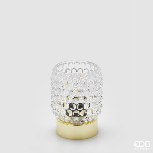 La lampada da tavolo Bubbles di Enzo De Gasperi (EDG) si distingue per un design raffinato che unisce un diffusore in vetro trasparente con un caratteristico motivo a rilievo a bolle e una base cilindrica in metallo dalla finitura dorata lucida. La particolare lavorazione del vetro permette alla luce di rifrangersi nell'ambiente in modo suggestivo, rendendo l'oggetto ideale come punto luce d'accento per spazi in stile Modern Luxury o Glamour.