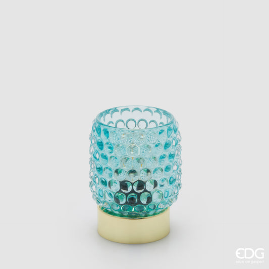 La lampada da tavolo Bubbles di Enzo De Gasperi (EDG) si distingue per un design raffinato che unisce un diffusore in vetro trasparente blu con un caratteristico motivo a rilievo a bolle e una base cilindrica in metallo dalla finitura dorata lucida. La particolare lavorazione del vetro permette alla luce di rifrangersi nell'ambiente in modo suggestivo, rendendo l'oggetto ideale come punto luce d'accento per spazi in stile Modern Luxury o Glamour.