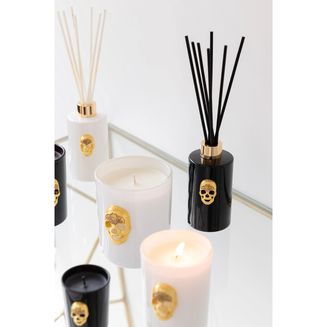 Diffusore di fragranza ad asta "Cranio" Nuit Noire firmato Jolipa, caratterizzato da una boccetta cilindrica in vetro nero lucido impreziosita da un dettaglio a rilievo dorato a forma di teschio e un colletto color oro abbinato. Questo esclusivo profumatore d'ambiente di design, completo di bastoncini neri, viene fornito con una raffinata confezione cilindrica coordinata total black con dettagli in oro, ideale per donare un tocco audace, moderno e sofisticato agli interni o come originale idea regalo