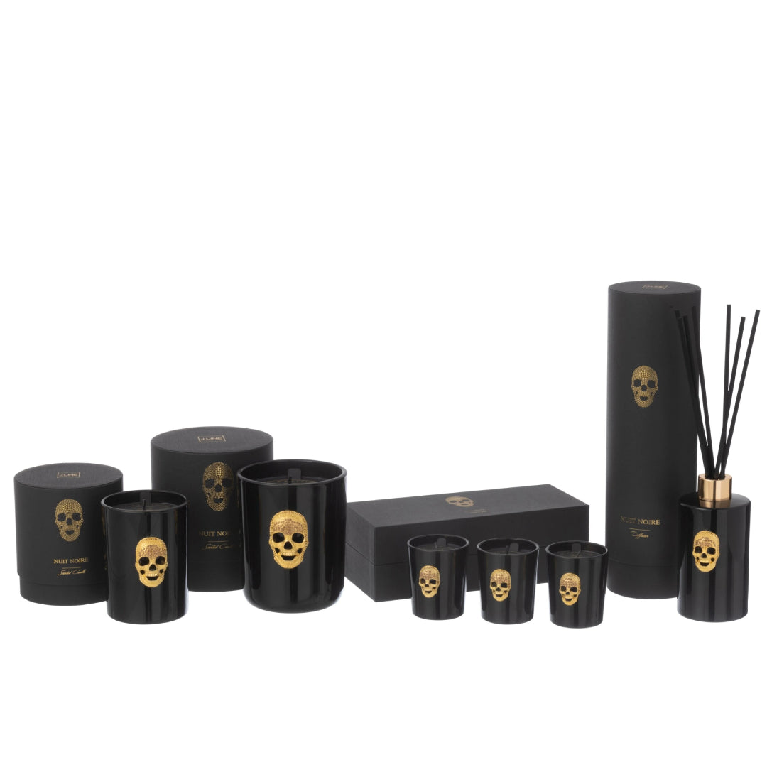 Collezione completa di candele profumate e diffusore d'ambiente a bastoncini "Cranio" Nuit Noire firmata Jolipa, caratterizzata da eleganti boccette e bicchieri in vetro nero lucido impreziositi da un teschio dorato in rilievo. Questa esclusiva linea di profumatori e candele decorative include scatole e confezioni regalo nere coordinate con dettagli in oro, perfetta come raffinata idea regalo o per impreziosire l'arredamento di interni moderni e di lusso.