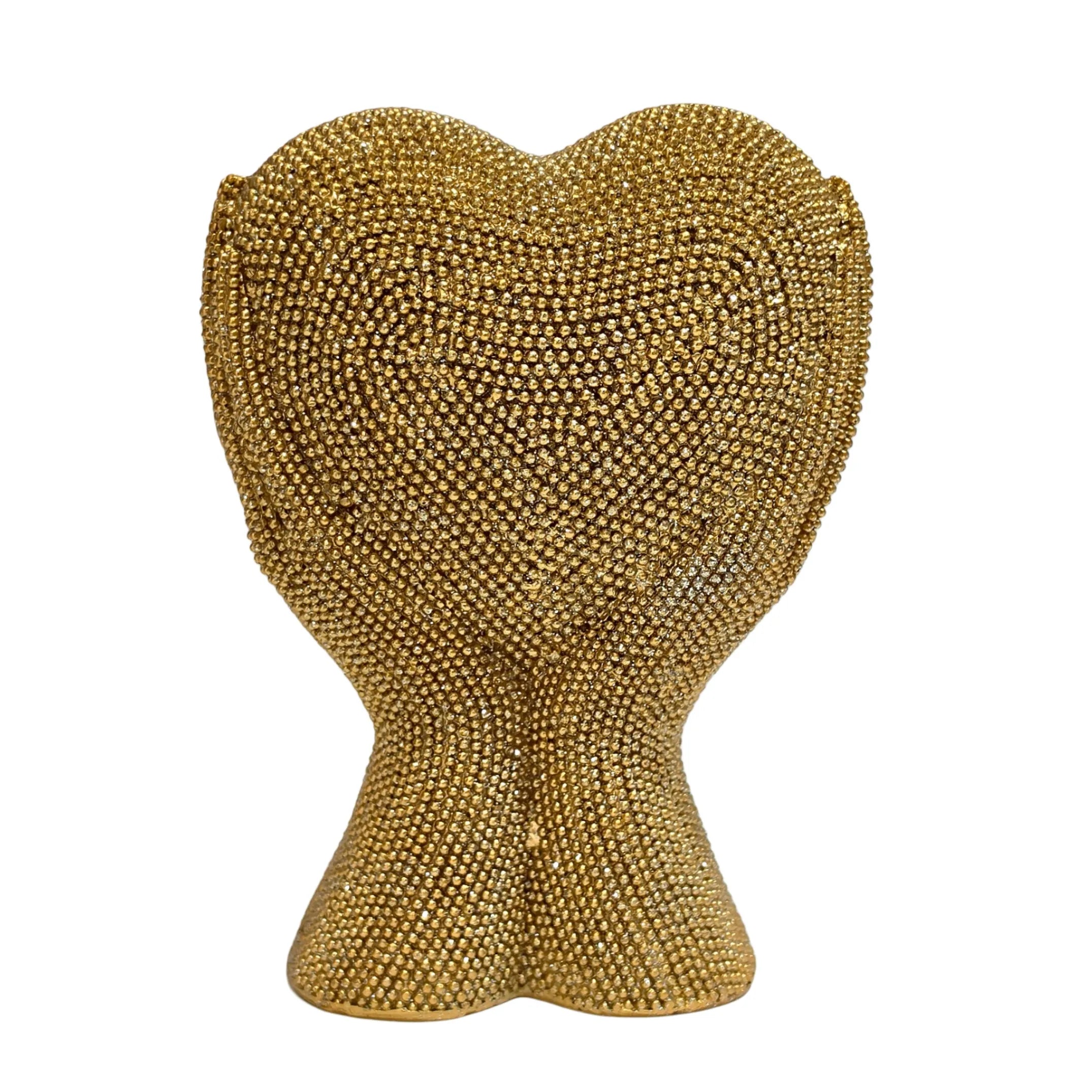 Statuina in resina raffigurante due mani dorate unite a formare un cuore visto frontalmente, interamente ricoperte di brillantini glitterati dall'effetto scintillante. Oggetto decorativo firmato Sud Import, ideale come soprammobile romantico o idea regalo per San Valentino e occasioni speciali.