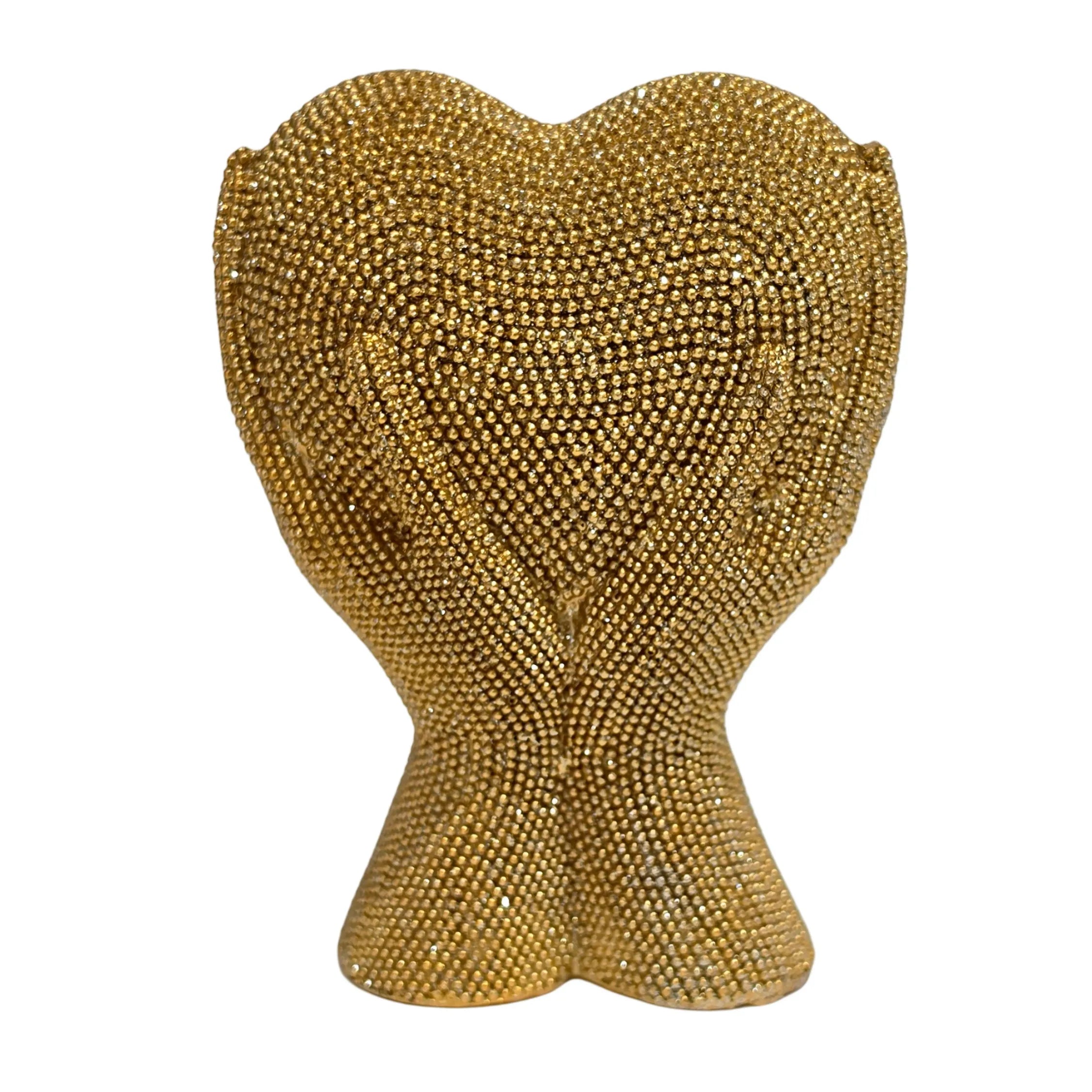 Statuina in resina raffigurante due mani dorate unite a formare un cuore visto frontalmente, interamente ricoperte di brillantini glitterati dall'effetto scintillante. Oggetto decorativo firmato Sud Import, ideale come soprammobile romantico o idea regalo per San Valentino e occasioni speciali.