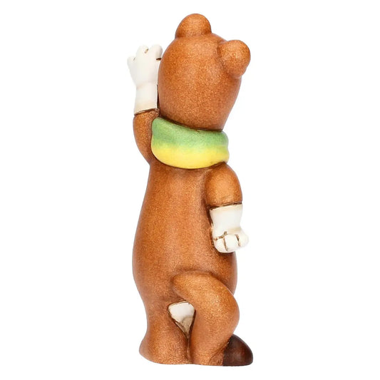 Vista posteriore della mascotte Milo Milano Cortina 2026. In risalto la colorazione bruna del manto, la zampa alzata in segno di saluto e il dettaglio della sciarpa sfumata.