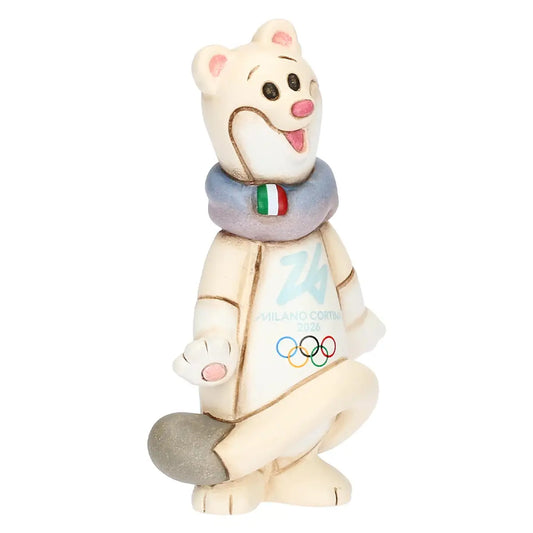 Vista a tre quarti della mascotte Tina Milano Cortina 2026. L'inquadratura esalta la posa dinamica dell'ermellino bianco e i dettagli colorati della sciarpa e dei simboli olimpici.