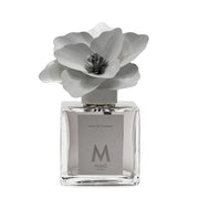 Profumatore d'ambiente Muhà Magnolia: flacone quadrato in vetro trasparente con essenza Fiori di Cotone e scenografico fiore in betulla color grigio.