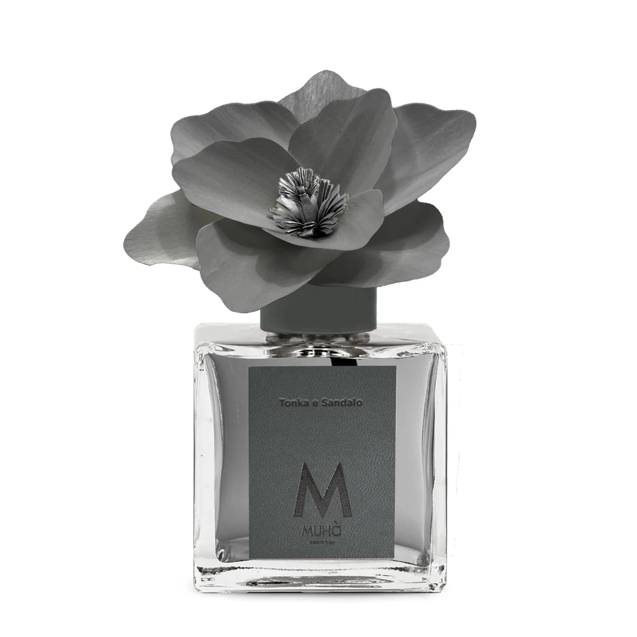 Profumatore d'ambiente Muhà Magnolia: flacone quadrato in vetro trasparente con essenza Tonka e Sandalo e scenografico fiore in betulla color antracite.