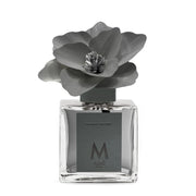 Profumatore d'ambiente Muhà Magnolia: flacone quadrato in vetro trasparente con essenza Tonka e Sandalo e scenografico fiore in betulla color antracite.